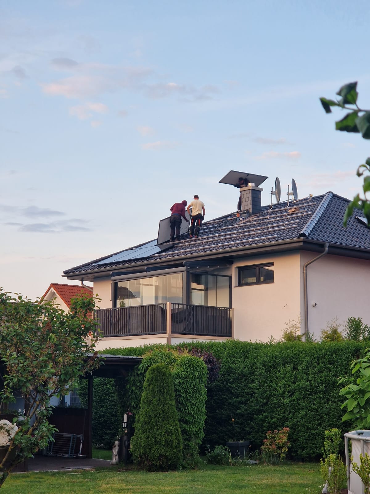 Drei Monteure tragen uhd installieren Solarmodule auf dem Dach eines Einfamilienhauses.