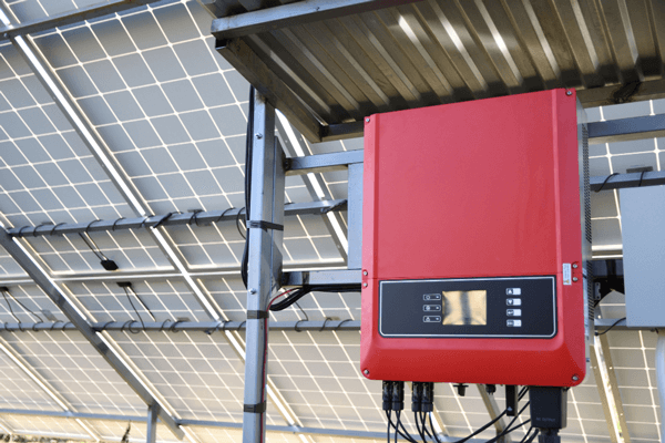 Roter Wechselrichterkasten, im Hintergrund die Rückseite von Solarmodulen